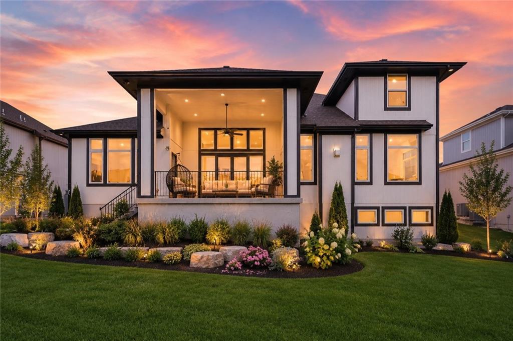 Rear elevation of 15620 Catalina St at dusk, the covered patio and interior glowing warm gold beneath a two-story wing, with landscaped beds along a manicured lawn