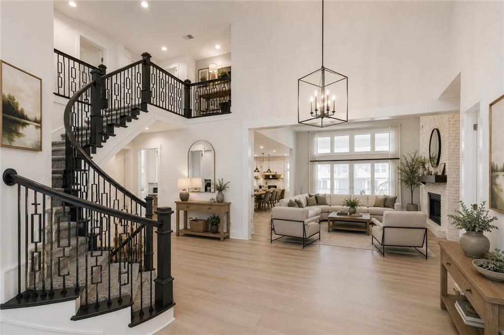Two-story great room of 15620 Catalina St, the curved staircase with dark iron balusters on the left, a cube-lantern chandelier overhead, and an open living, dining, and kitchen beyond