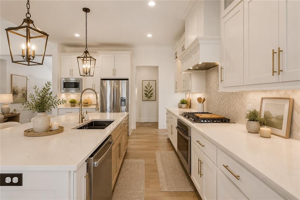 Gourmet kitchen with a long quartz waterfall island and farmhouse sink, white shaker cabinets with brass hardware, brass lantern pendants, gas cooktop, and herringbone tile backsplash