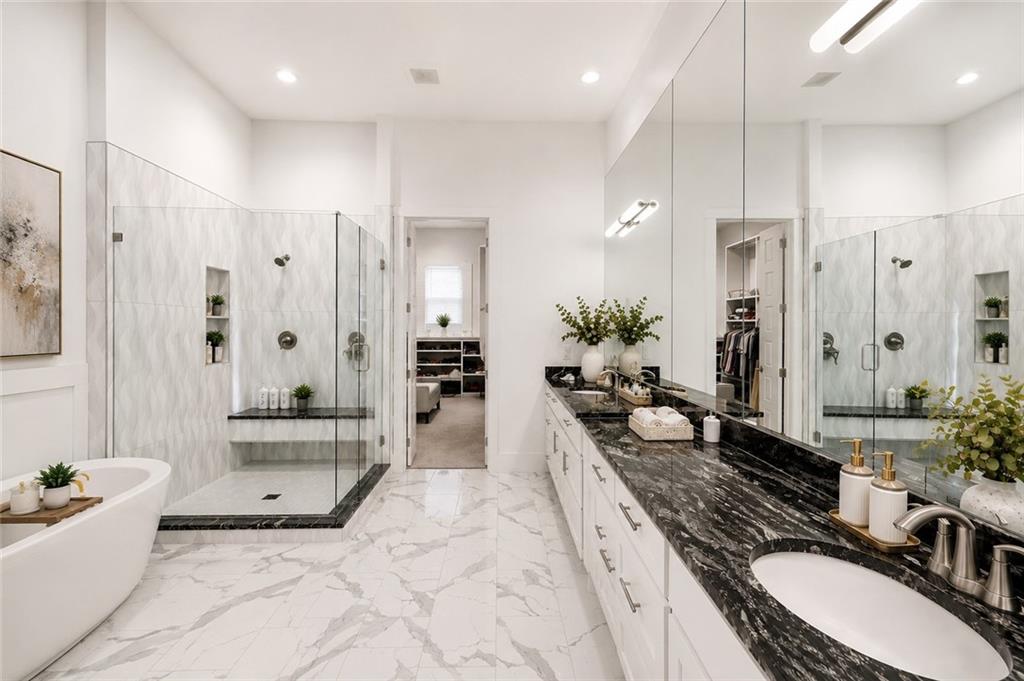 Primary bath with a freestanding soaking tub, a glass walk-in shower with a bench and rippled tile, a double vanity topped in dark veined marble, and a marble tile floor opening to the closet