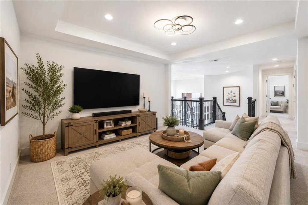 Upstairs loft retreat with a tray ceiling, a wall-mounted TV on a wood media console, a plush sectional, and the iron stair railing overlooking the level below